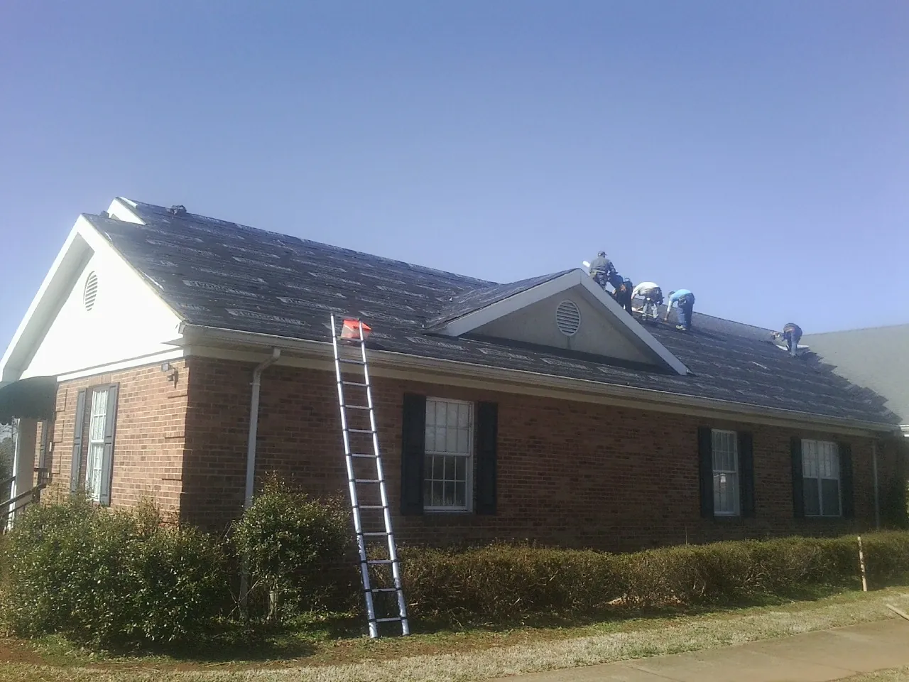 Crew tearing shingles off a brick ranch roof with a ladder set — Metal Roof Repair work by our crew in Carthage