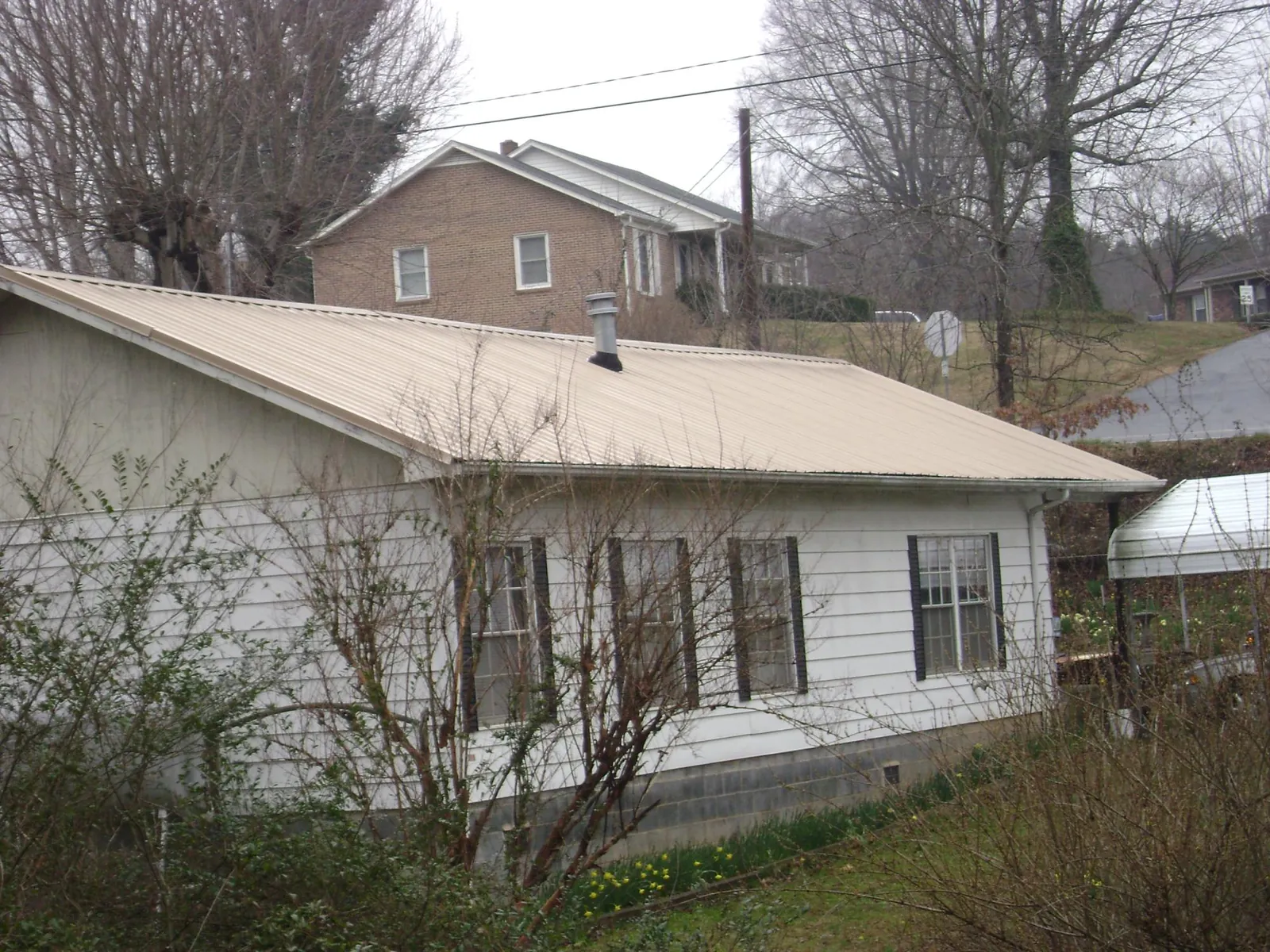 Tan metal roof on a white sided house set into a hillside — Commercial Roofing by Roofing Brothers in Carthage